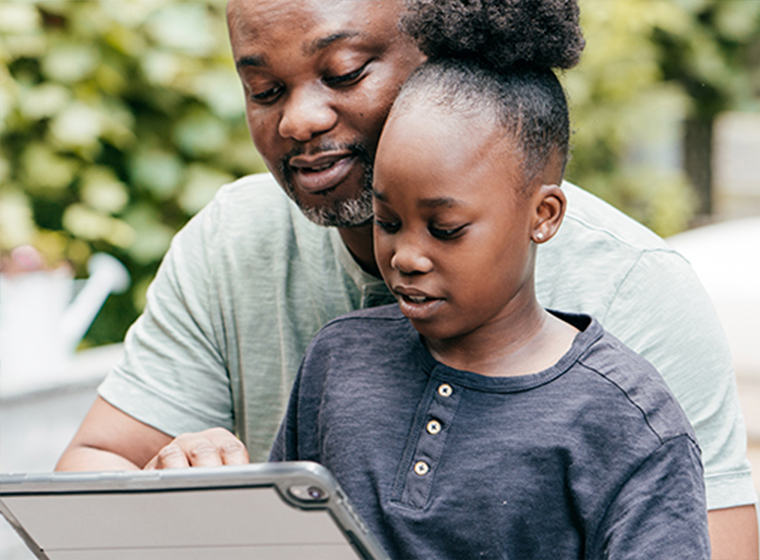 A parent siting with his child pointing to a laptop.