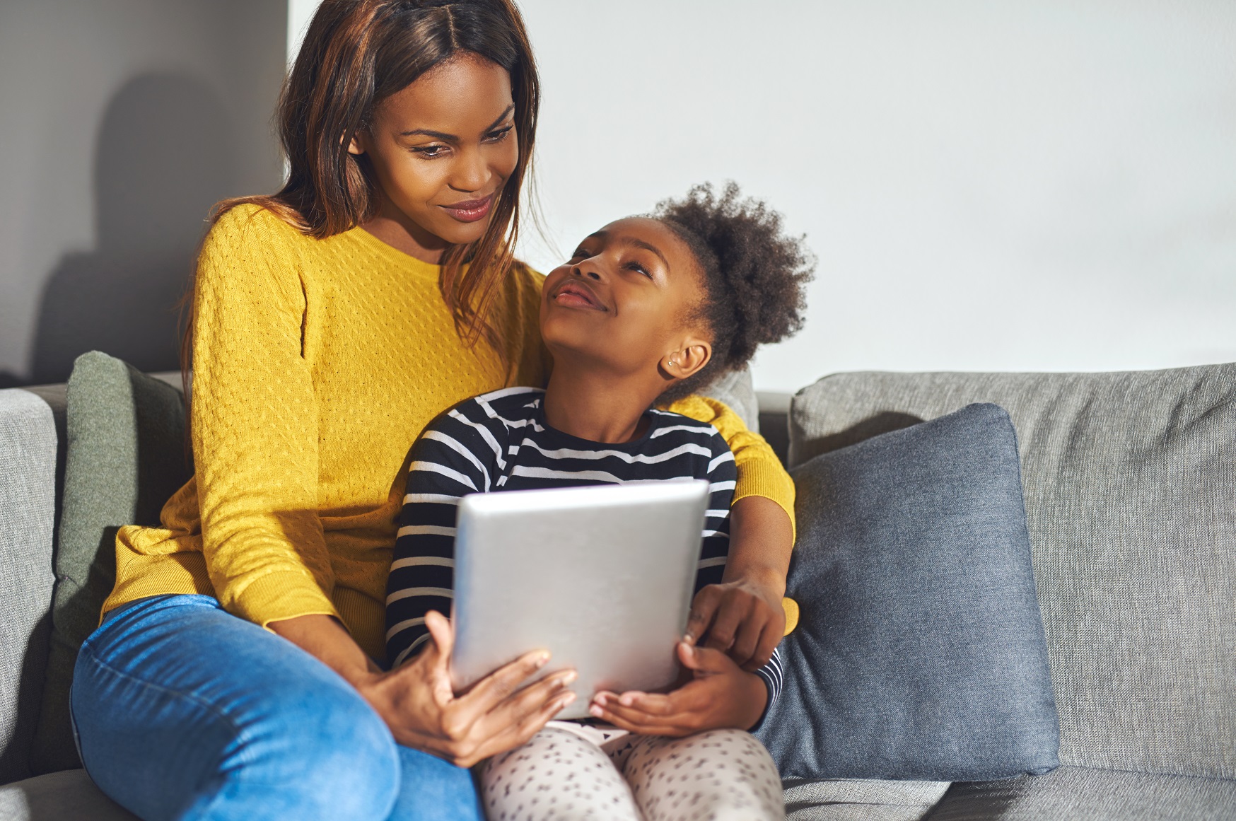 A person and a child sitting on a couch looking at a tablet