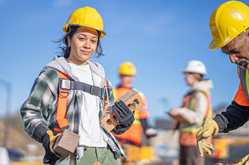 Une jeune élève portant un équipement de protection travaille sur un chantier de construction. 