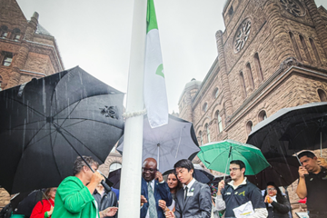 Officials and attendees gathered outdoors raising the Franco-Ontarian flag during a ceremony at Queen’s Park.