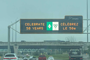 Highway electronic sign displaying a message celebrating the 50th anniversary of the Franco-Ontarian flag above a roadway.