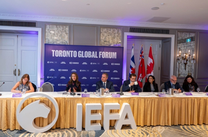 Photograph of Ontario’s Minister of Francophone Affairs, the Honourable Caroline Mulroney, seated at a long table with Jean‑Claude D’Amours, New Brunswick Cabinet Minister, during the Toronto Global Forum, along with other representatives. A large sign displaying the letters “IEFA” is positioned in front of the table.