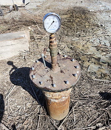 A pipe sticking out of the ground with a circular metal cover screwed on the top of the pipe.